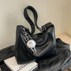 Black handbag with a fluffy keychain on a textured surface