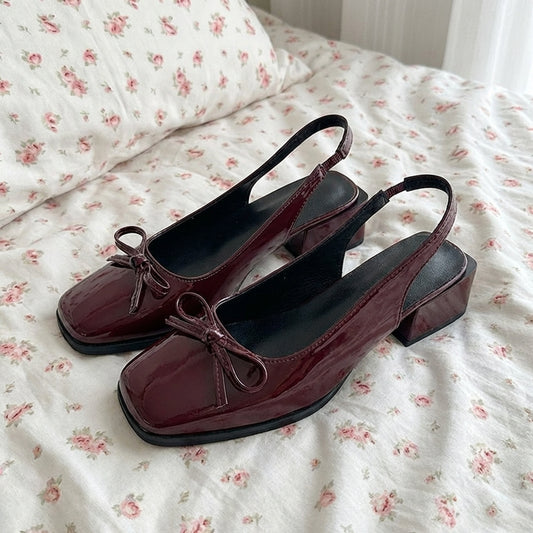Pair of maroon shoes with black soles on a floral bedspread