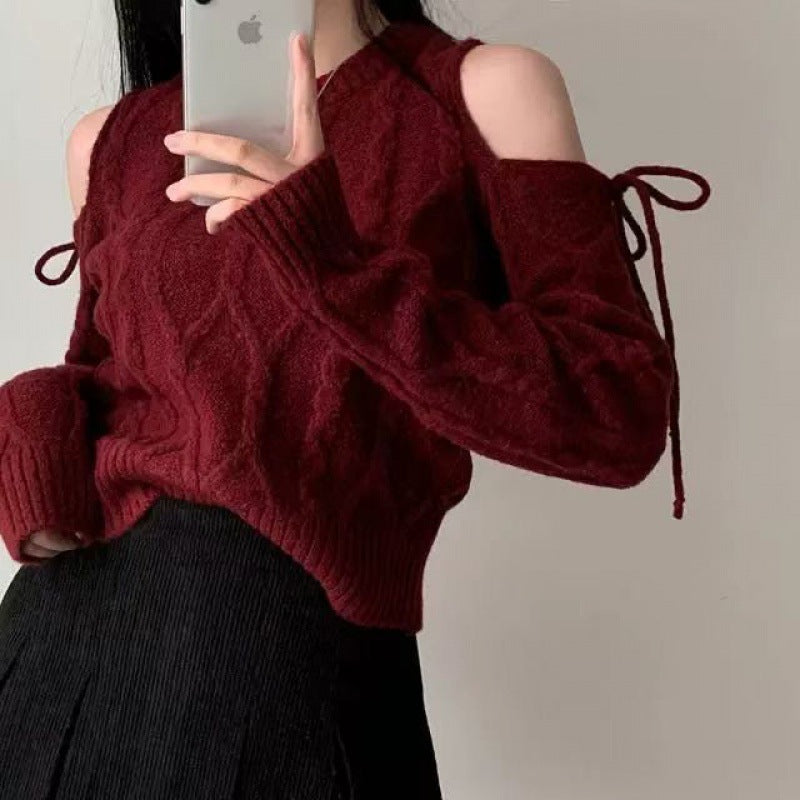 Person wearing a burgundy knitted sweater with cut-out shoulders against a plain background