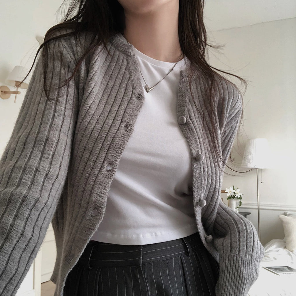 Person wearing a gray cardigan over a white shirt in a bedroom setting