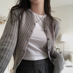 Person wearing a gray cardigan over a white shirt in a bedroom setting