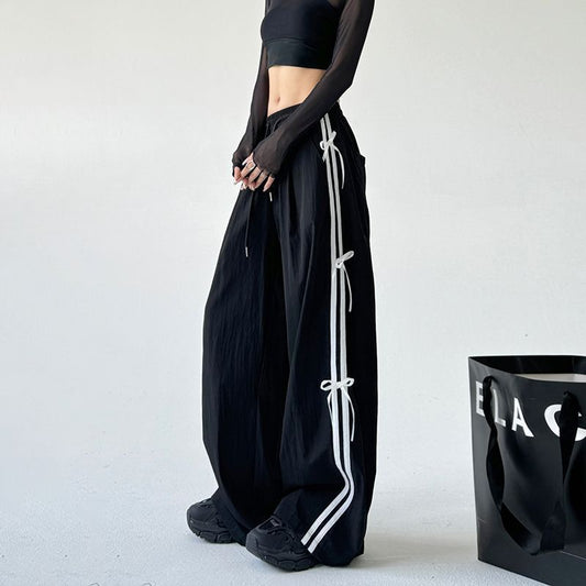 Person wearing black pants with white stripes standing next to a black bag on a light gray background