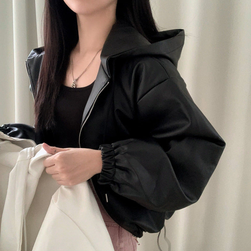 Person wearing a black jacket holding a white garment against a neutral background