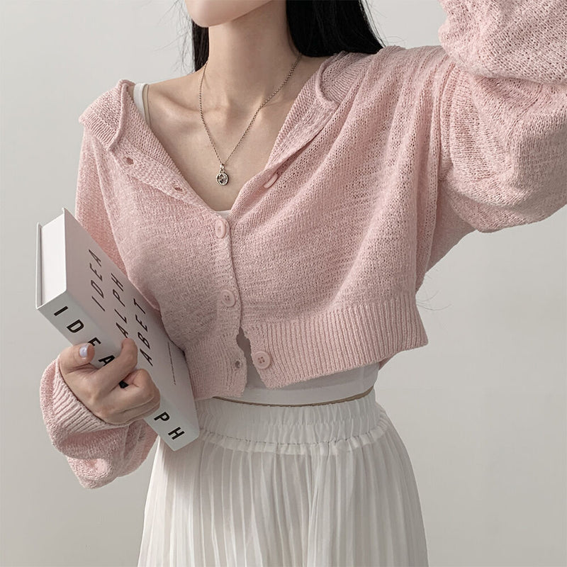 Person wearing a pink knitted cardigan holding a book against a plain background