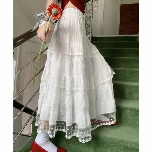 Person wearing a white lace skirt with red shoes and holding a flower on a staircase.