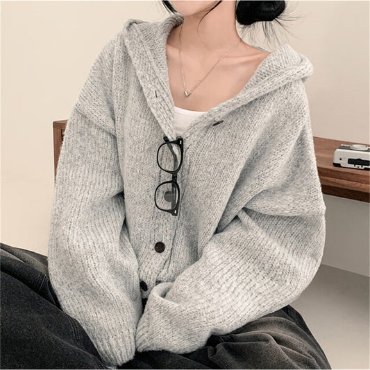 Person wearing a gray knitted cardigan with glasses on a wooden surface