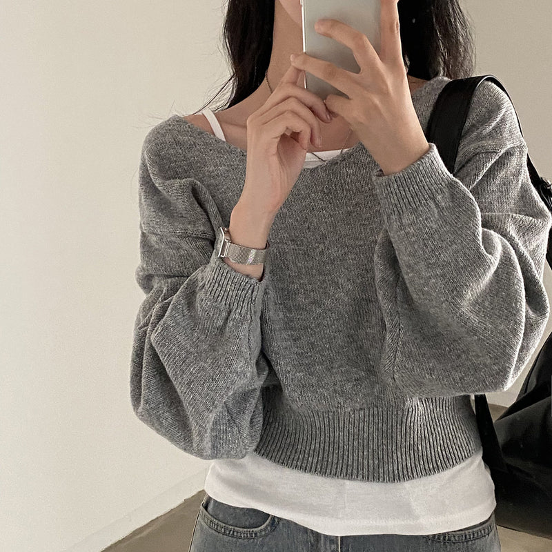 Person wearing a gray sweater with balloon sleeves, taking a selfie.