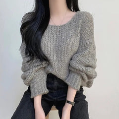 Person wearing a chunky knit sweater and dark pants against a plain background