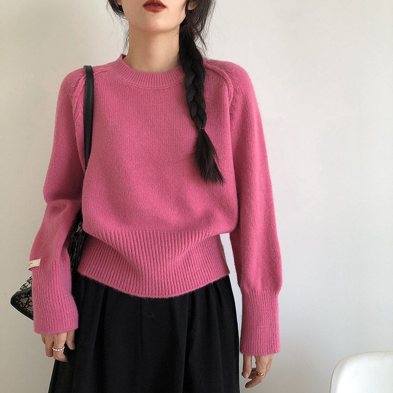 Person wearing a pink sweater and black skirt against a plain background