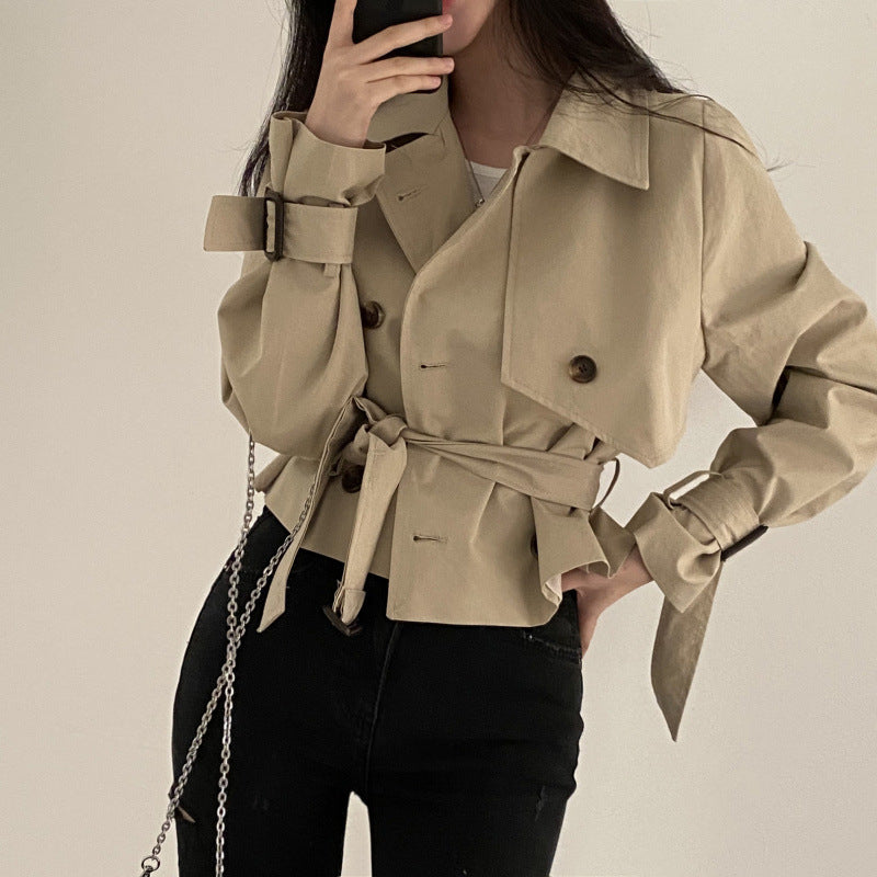 Person wearing a beige trench coat with a neutral background