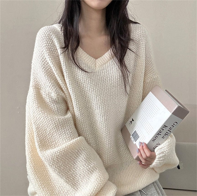 Person wearing a cream knitted sweater holding a book against a neutral background