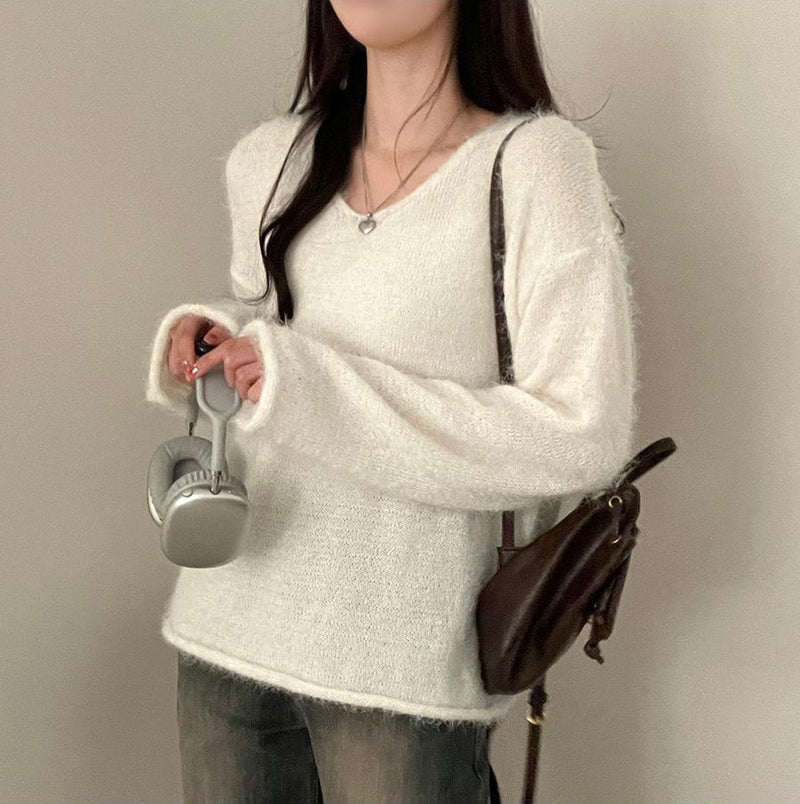 Person wearing a white textured sweater holding a silver object against a plain background