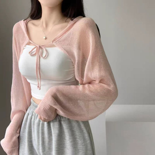 Woman wearing a pink cardigan over a white top and gray pants against a neutral background