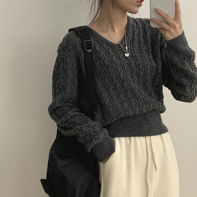 Person wearing a dark gray cable knit sweater and light-colored pants against a neutral background