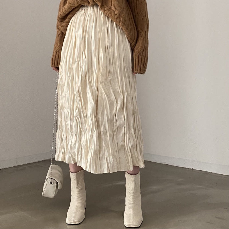 Person wearing a beige pleated skirt and white boots in a minimalistic setting