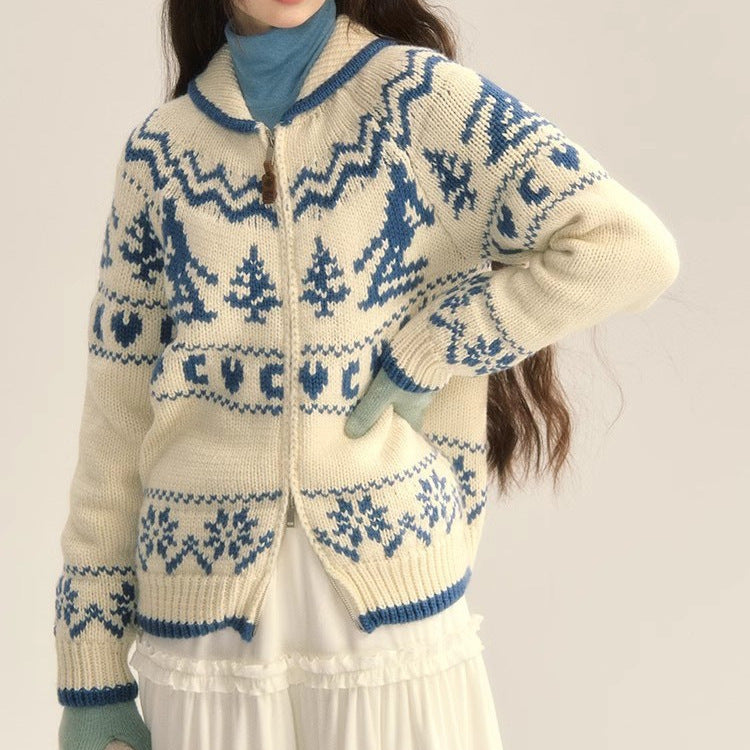 Person wearing a cream and blue patterned sweater with matching gloves on a plain background
