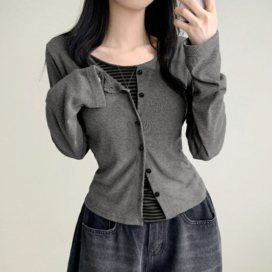 Person wearing a gray cardigan over a striped shirt with a plain background