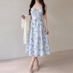 Woman wearing a blue floral dress holding a white cardigan against a plain background