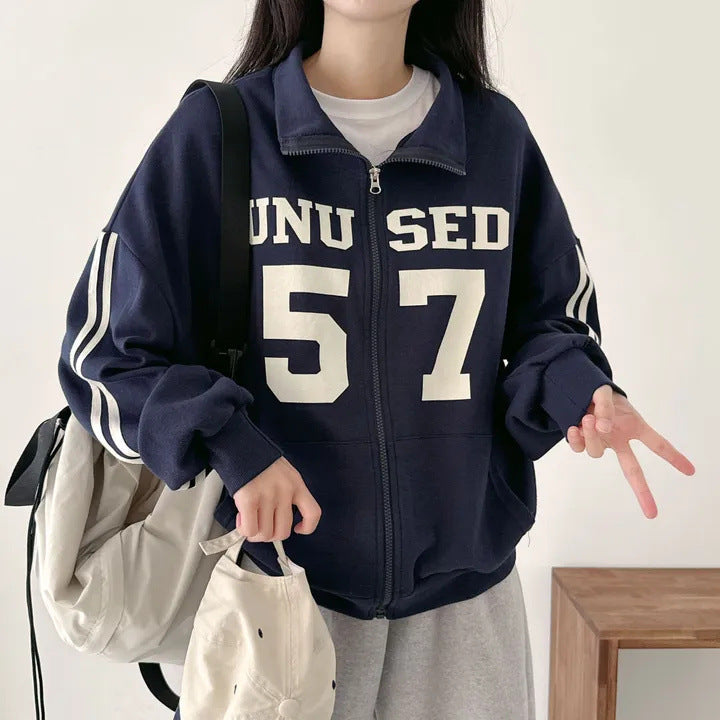 Person wearing a navy blue jacket with 'UNISED 57' text, holding bags indoors.