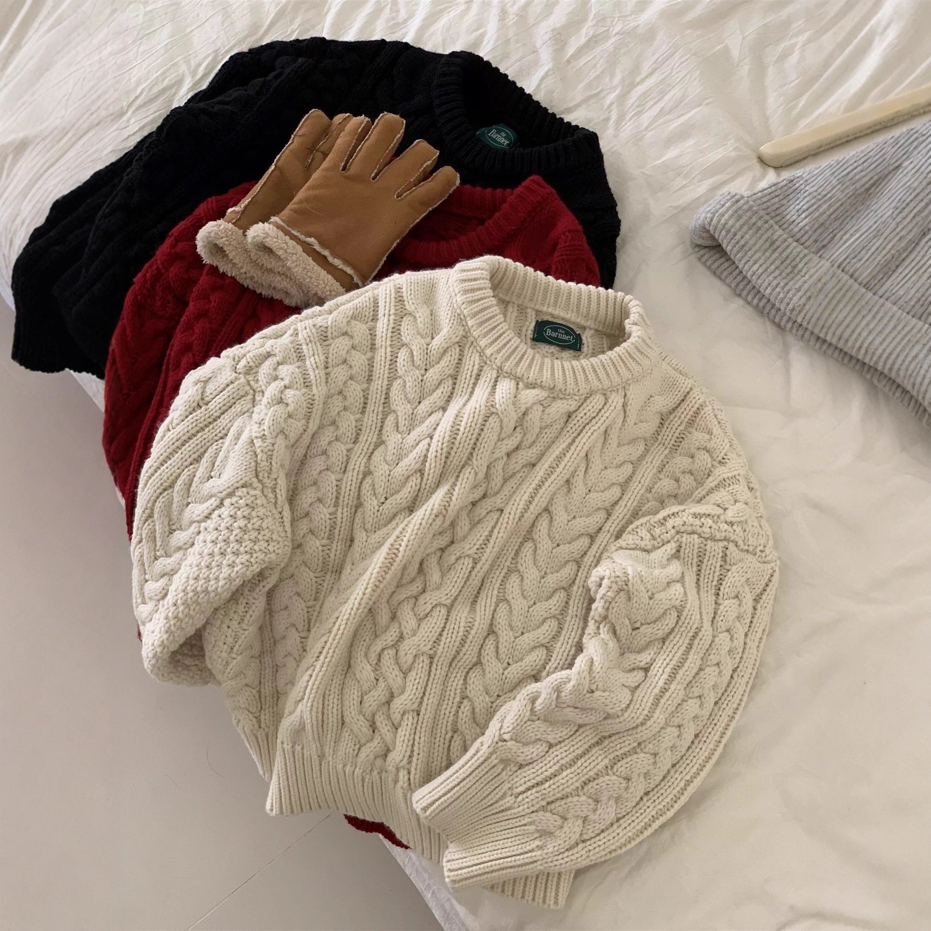 Folded cream sweater with cable knit pattern on a white surface