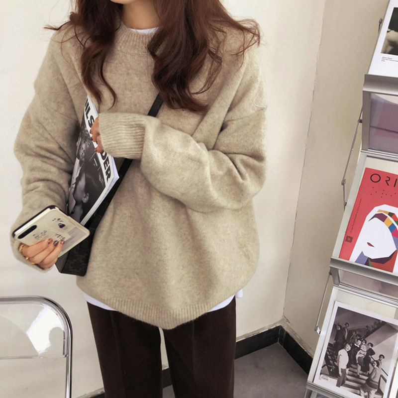 Person wearing a beige sweater holding a magazine in an indoor setting.