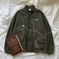 An olive green corduroy jacket is laid flat on white fabric, styled with a book titled 'One Hundred Years of Solitude' by Gabriel García Marquez and white wired earbuds.