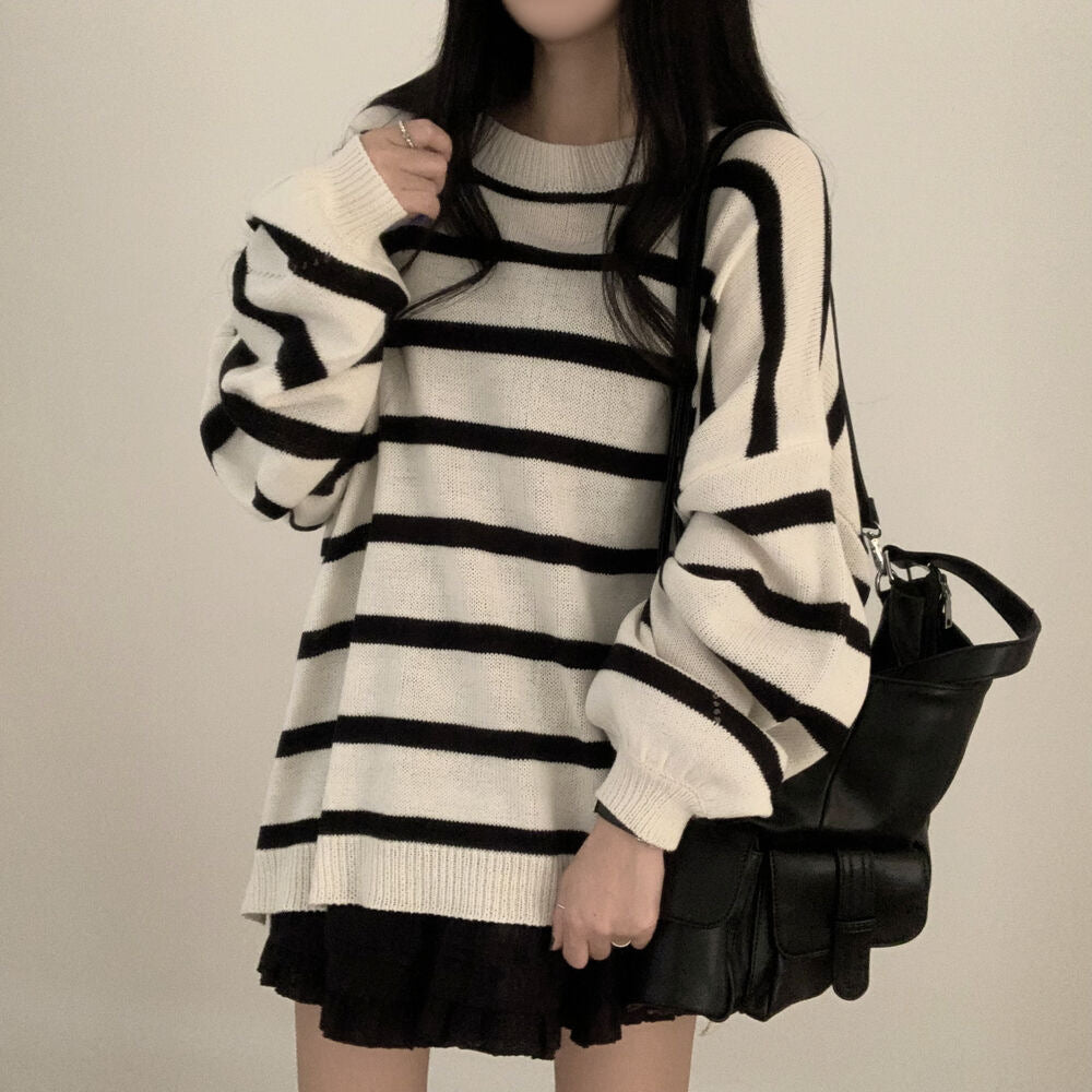 Person wearing a black and white striped sweater over a dress, holding a black handbag on a plain background