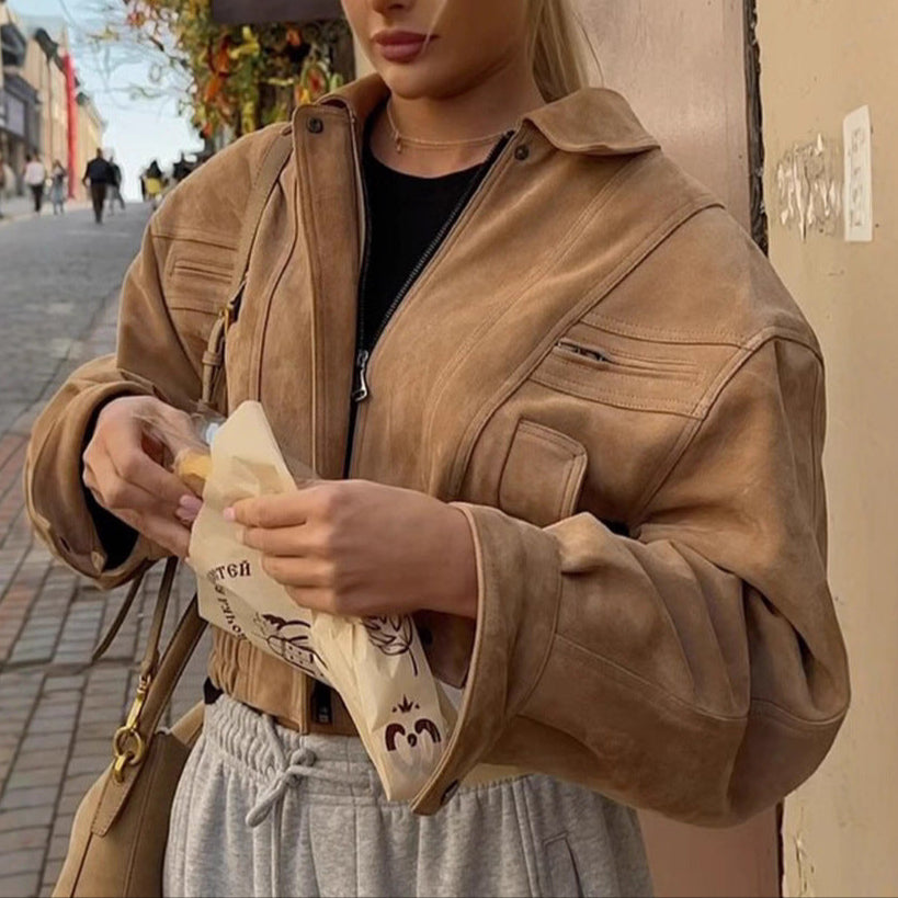 Person wearing a brown jacket holding a bag with a brand logo on a street.