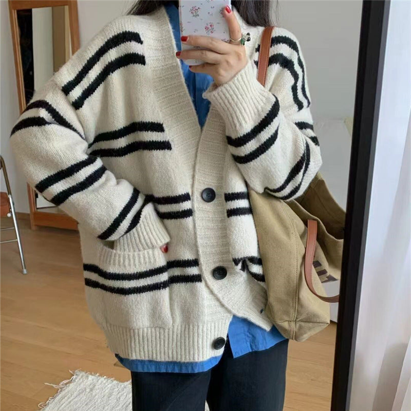 Person wearing a white cardigan with black stripes and buttons, holding a phone.