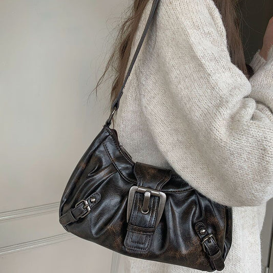 Person wearing a white sweater holding a black leather handbag.
