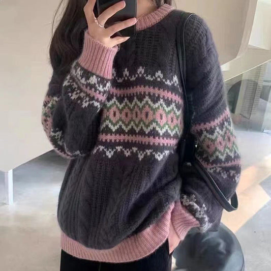 A person wearing a dark charcoal gray knit sweater with a pink and white Fair Isle pattern across the chest and sleeves, paired with black pants and a black shoulder bag.